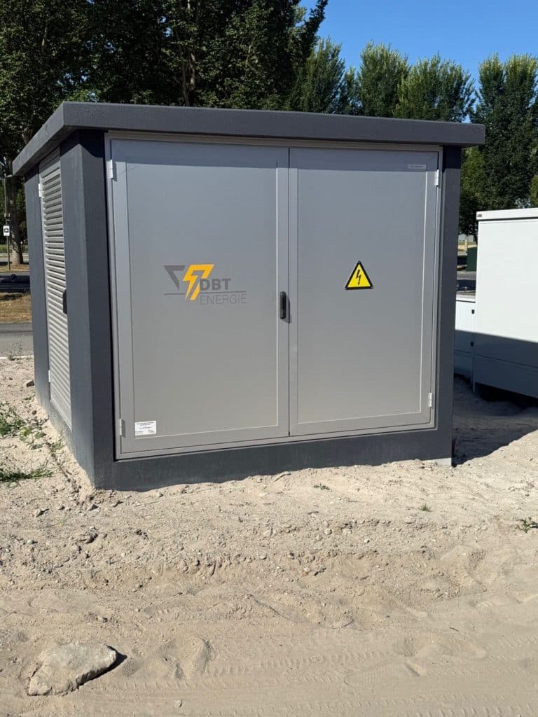 Compactstation van DBT Energie in antraciet met dubbele aluminium deuren, geplaatst op een terrein